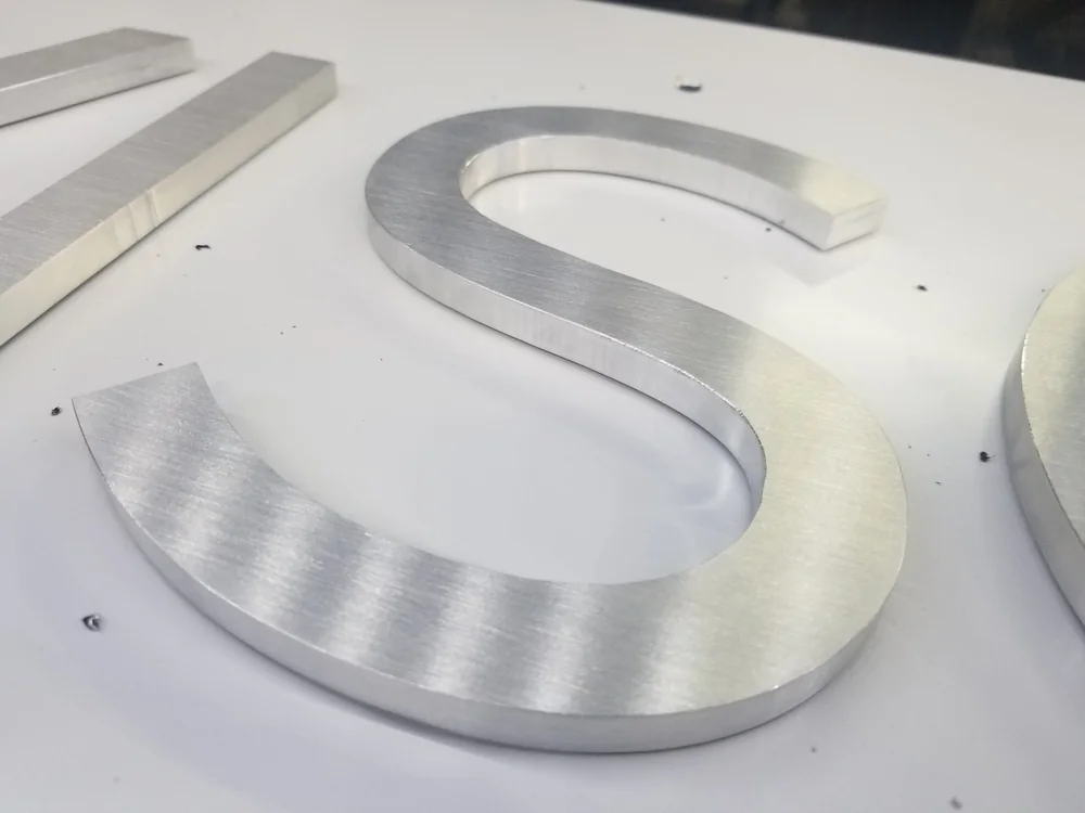 Machined flat-cut metal letter shown for construction comparison